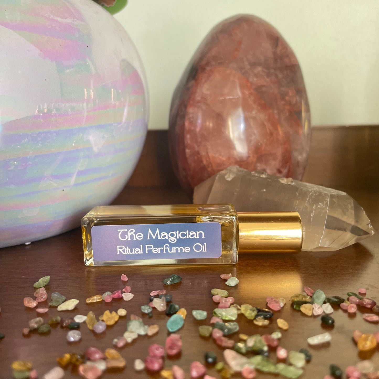 Perfume oil bottle labeled 'The Magician' with crystals and stones on a neutral background